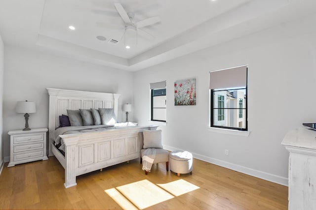 bedroom with a raised ceiling, ceiling fan, and light wood-type flooring