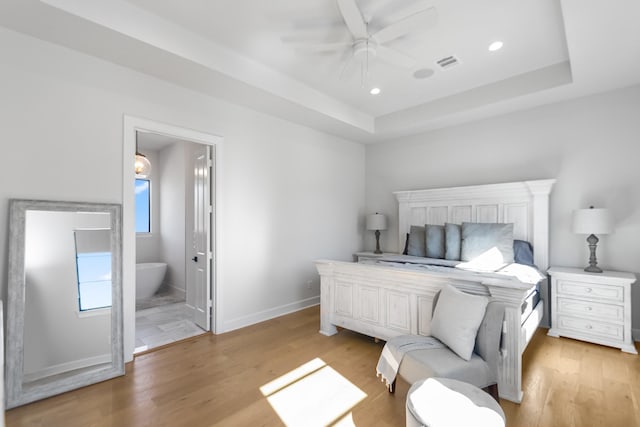 bedroom featuring ceiling fan, ensuite bathroom, a raised ceiling, and light hardwood / wood-style flooring