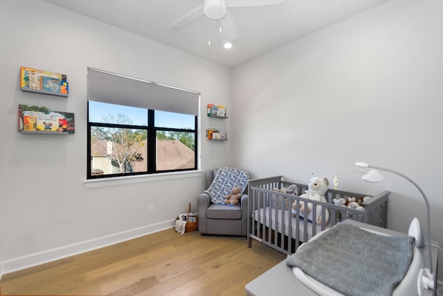 bedroom with a nursery area, ceiling fan, and light hardwood / wood-style floors