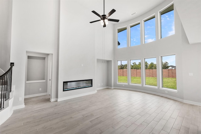 unfurnished living room featuring plenty of natural light, ceiling fan, and a high ceiling