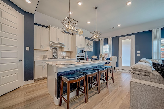 kitchen with a center island with sink, decorative light fixtures, light hardwood / wood-style floors, and white cabinetry