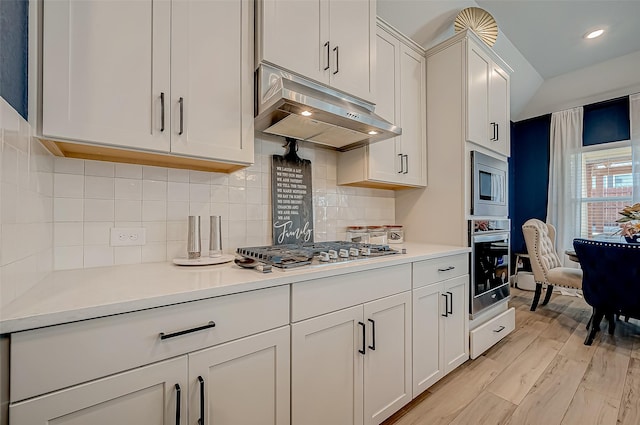 kitchen with white cabinets, decorative backsplash, stainless steel appliances, and light hardwood / wood-style floors