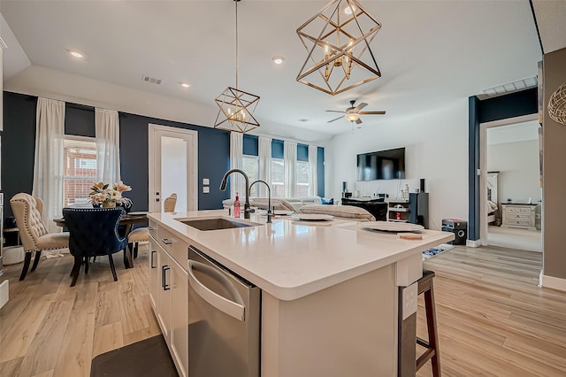 kitchen featuring sink, dishwasher, a kitchen breakfast bar, pendant lighting, and a kitchen island with sink