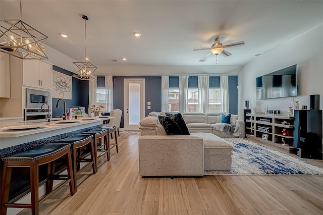 living room with sink, ceiling fan with notable chandelier, and light wood-type flooring