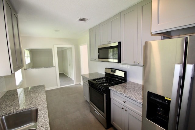 kitchen featuring light stone countertops, a textured ceiling, stainless steel appliances, and backsplash