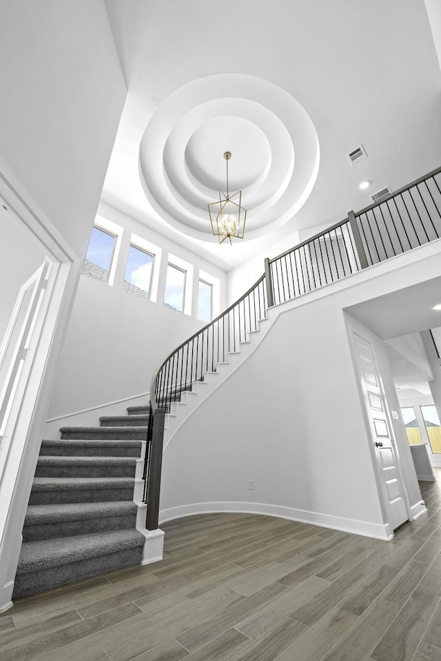 staircase with a raised ceiling, a towering ceiling, and a chandelier