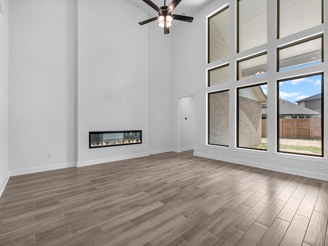 3248 Stingray Cove Dr, Katy, TX 77493 - unfurnished living room featuring wood finished floors, a towering ceiling, a ceiling fan, baseboards, and a glass covered fireplace