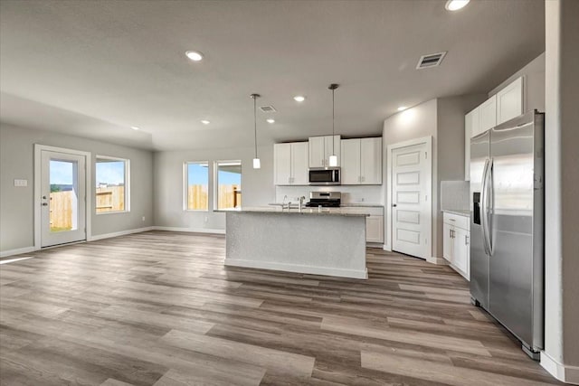 kitchen featuring white cabinets, stainless steel appliances, hanging light fixtures, and a center island with sink