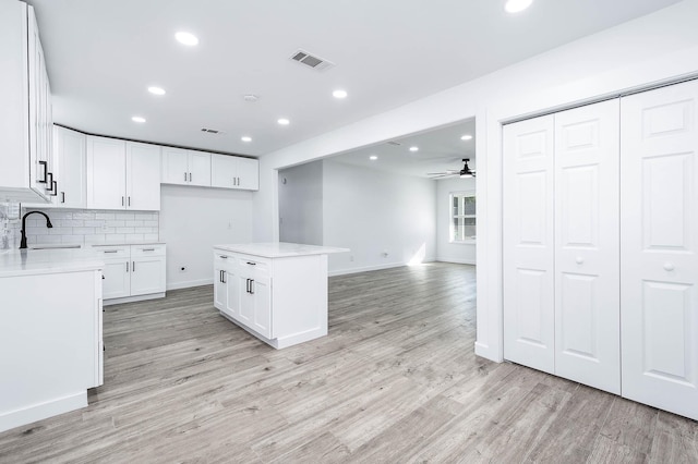 kitchen with light wood-type flooring, ceiling fan, sink, white cabinets, and a kitchen island