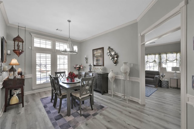 dining space with light wood-type flooring, ornamental molding, and an inviting chandelier