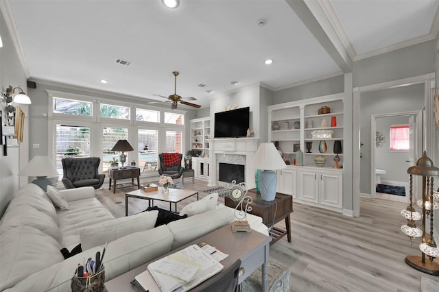 living room featuring built in shelves, light hardwood / wood-style floors, ceiling fan, and crown molding