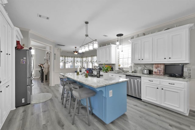 kitchen with appliances with stainless steel finishes, ceiling fan, pendant lighting, white cabinets, and a kitchen island