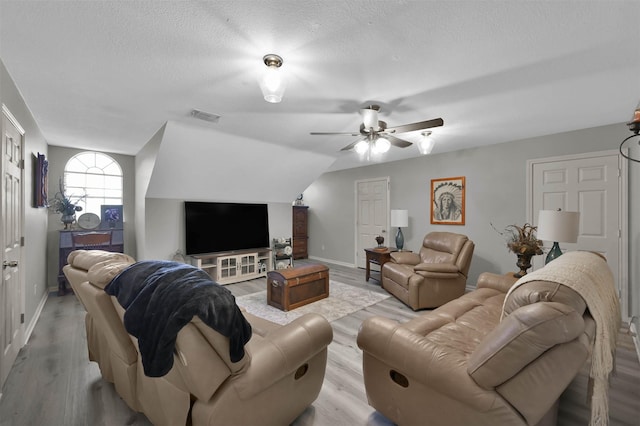 living room with a textured ceiling, ceiling fan, light hardwood / wood-style flooring, and lofted ceiling