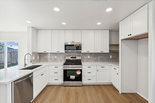 kitchen featuring appliances with stainless steel finishes, light wood-type flooring, tasteful backsplash, sink, and white cabinetry