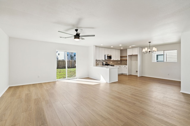 unfurnished living room with plenty of natural light, ceiling fan with notable chandelier, and light wood-type flooring