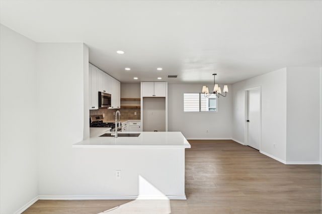 kitchen with white cabinets, appliances with stainless steel finishes, tasteful backsplash, kitchen peninsula, and a chandelier