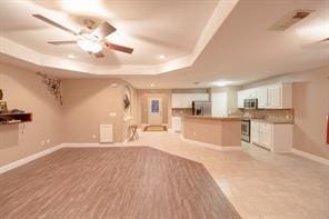 unfurnished living room featuring a raised ceiling and ceiling fan