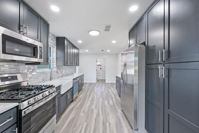 kitchen featuring sink, light stone counters, light hardwood / wood-style floors, decorative backsplash, and appliances with stainless steel finishes