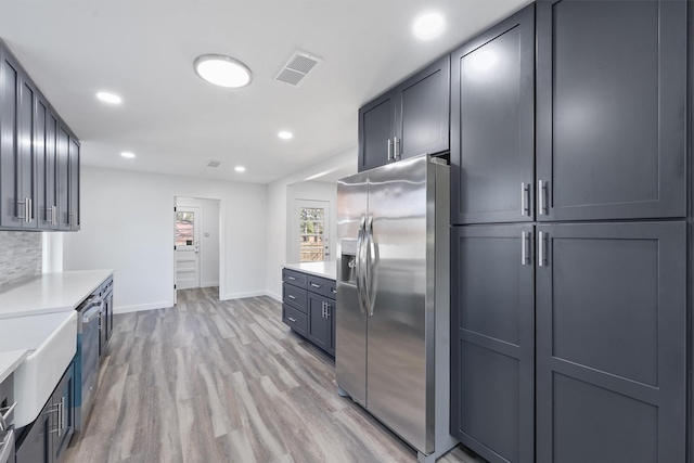 kitchen with light wood-type flooring, stainless steel fridge with ice dispenser, gray cabinetry, and decorative backsplash