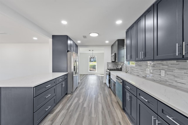 kitchen with appliances with stainless steel finishes, light hardwood / wood-style floors, pendant lighting, light stone counters, and tasteful backsplash