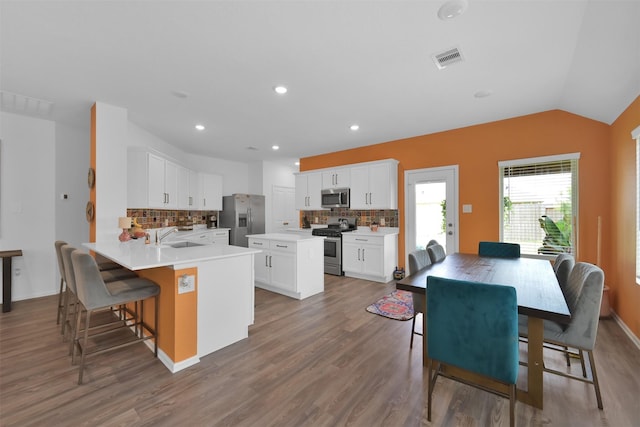 kitchen featuring kitchen peninsula, appliances with stainless steel finishes, decorative backsplash, white cabinetry, and lofted ceiling