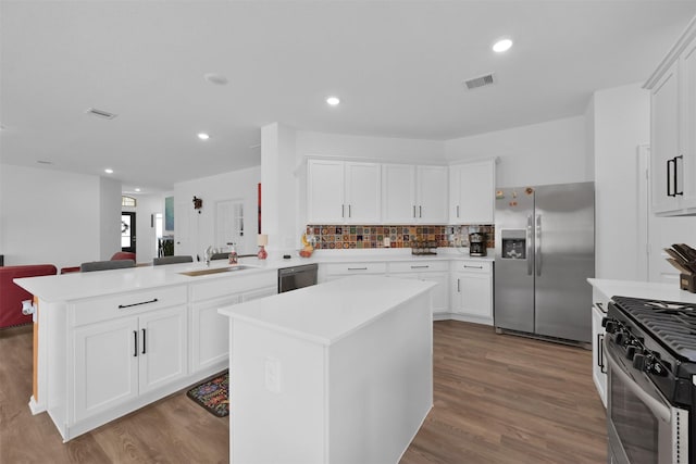 kitchen featuring kitchen peninsula, stainless steel appliances, sink, white cabinets, and a center island