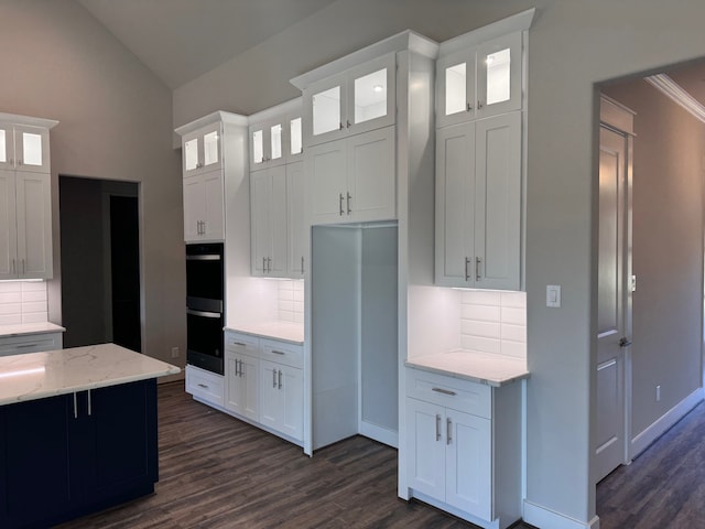 kitchen with backsplash, white cabinetry, light stone counters, and vaulted ceiling