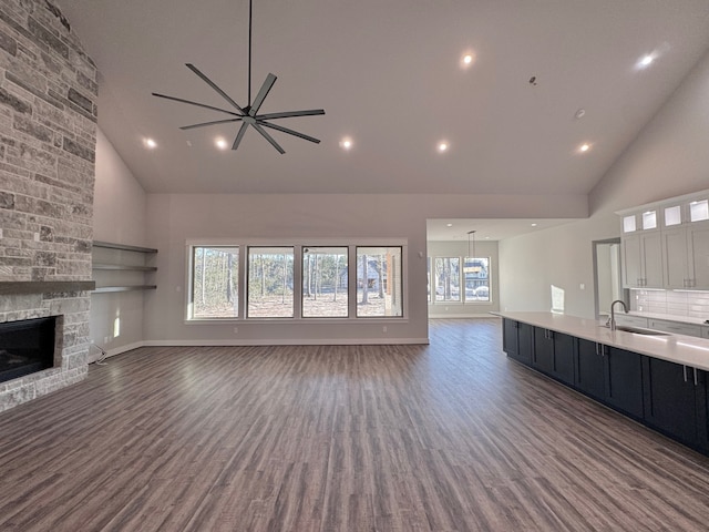 unfurnished living room featuring ceiling fan, sink, high vaulted ceiling, dark hardwood / wood-style floors, and a stone fireplace