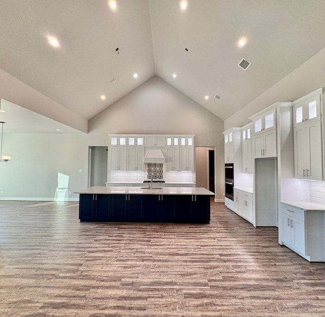 kitchen with a large island with sink, high vaulted ceiling, tasteful backsplash, and white cabinetry