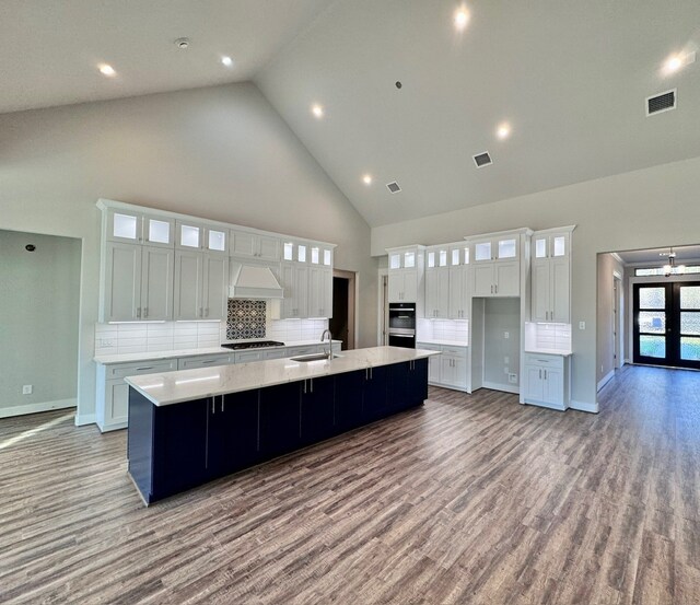 kitchen with white cabinetry, sink, high vaulted ceiling, a large island with sink, and wood-type flooring