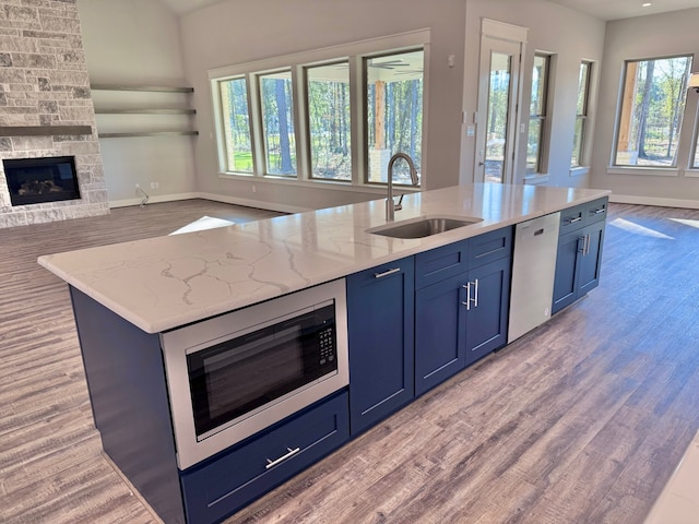 kitchen featuring sink, stainless steel appliances, light stone counters, an island with sink, and a fireplace