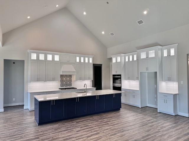 kitchen with premium range hood, high vaulted ceiling, a large island, light hardwood / wood-style floors, and white cabinetry