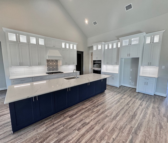 kitchen with sink, black gas cooktop, high vaulted ceiling, a large island with sink, and custom range hood