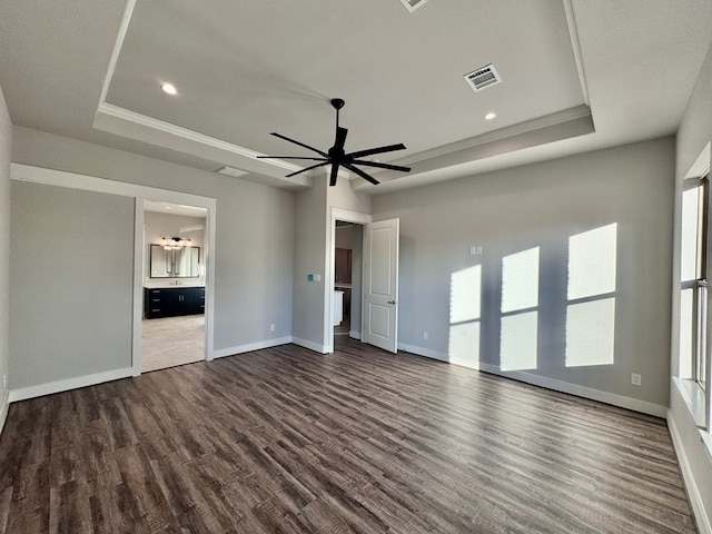 unfurnished bedroom featuring a tray ceiling, ensuite bath, ceiling fan, and dark wood-type flooring