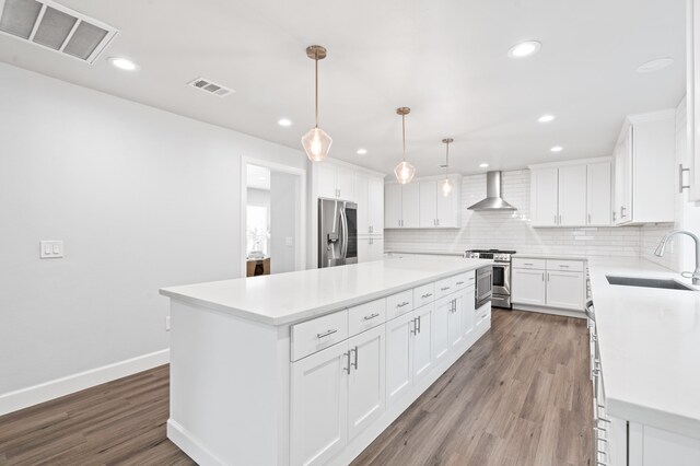 kitchen featuring appliances with stainless steel finishes, wall chimney exhaust hood, sink, a center island, and white cabinetry