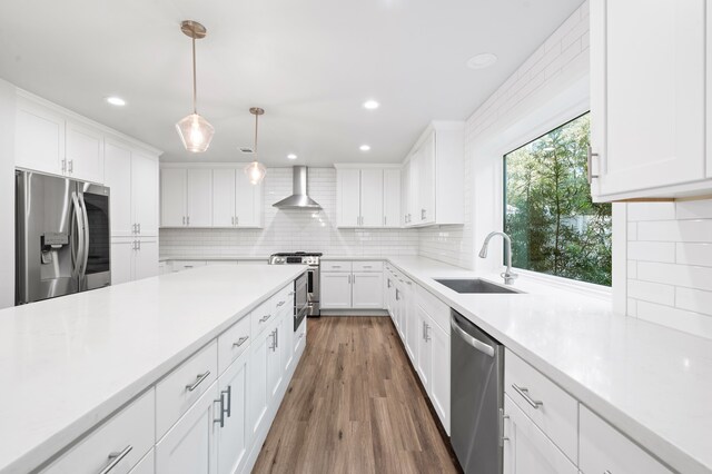 kitchen featuring appliances with stainless steel finishes, wall chimney exhaust hood, sink, pendant lighting, and white cabinetry