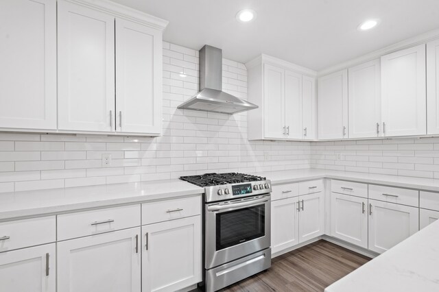 kitchen with white cabinets, stainless steel stove, light stone counters, and wall chimney range hood