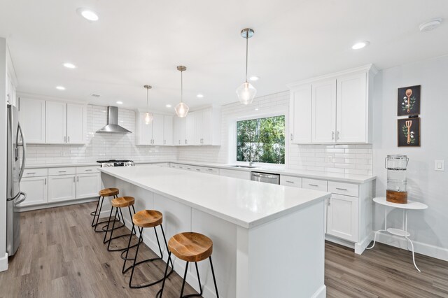 kitchen featuring appliances with stainless steel finishes, wall chimney exhaust hood, white cabinetry, light hardwood / wood-style flooring, and a kitchen island