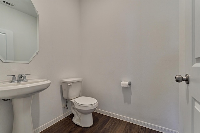 half bath with toilet, a sink, wood finished floors, visible vents, and baseboards