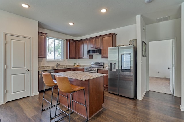 kitchen featuring a center island, sink, dark hardwood / wood-style floors, light stone countertops, and appliances with stainless steel finishes