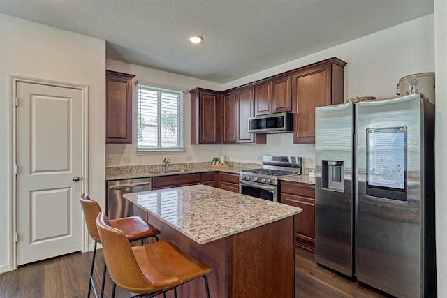 kitchen with a center island, sink, dark wood-type flooring, stainless steel appliances, and light stone counters