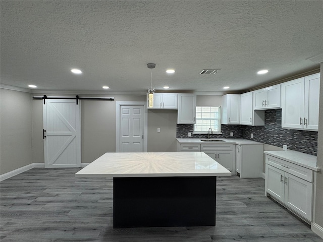 kitchen with white cabinetry, a center island, a barn door, crown molding, and pendant lighting