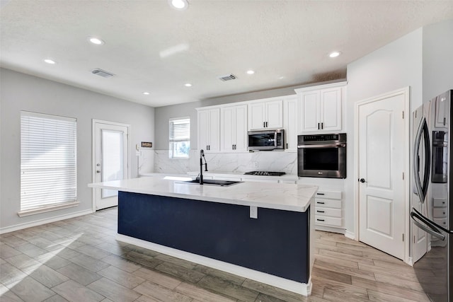 kitchen featuring sink, white cabinetry, light stone countertops, a center island with sink, and appliances with stainless steel finishes