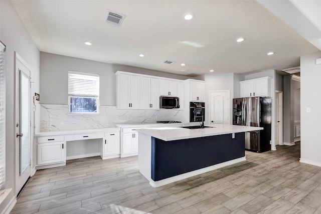 kitchen with a center island with sink, white cabinetry, backsplash, and appliances with stainless steel finishes