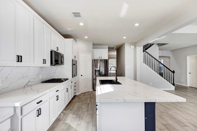 kitchen with stainless steel appliances, sink, light stone counters, tasteful backsplash, and an island with sink