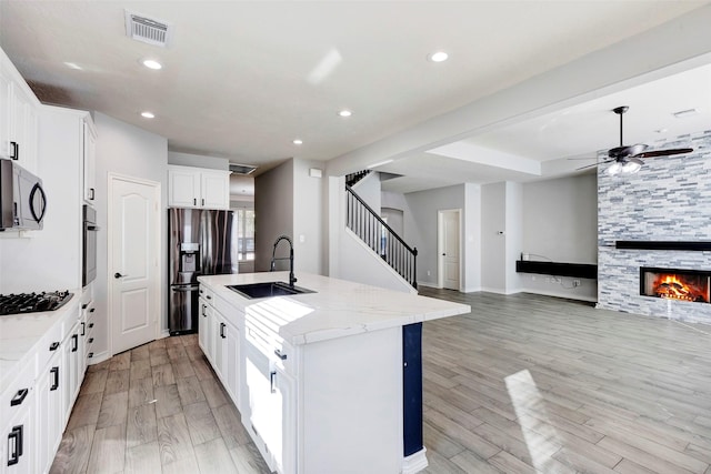 kitchen with sink, stainless steel appliances, white cabinets, light wood-type flooring, and a kitchen island with sink