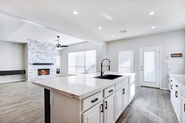 kitchen with sink, a fireplace, white cabinetry, light stone countertops, and a kitchen island with sink