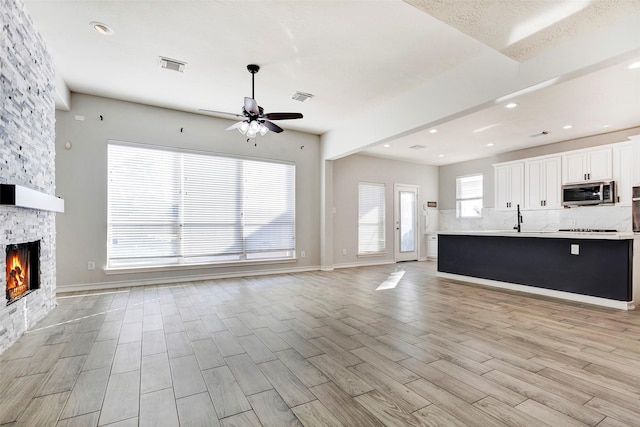 unfurnished living room with a healthy amount of sunlight, ceiling fan, sink, and a fireplace