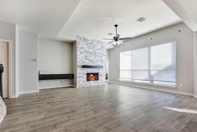 unfurnished living room with ceiling fan, a stone fireplace, and a textured ceiling