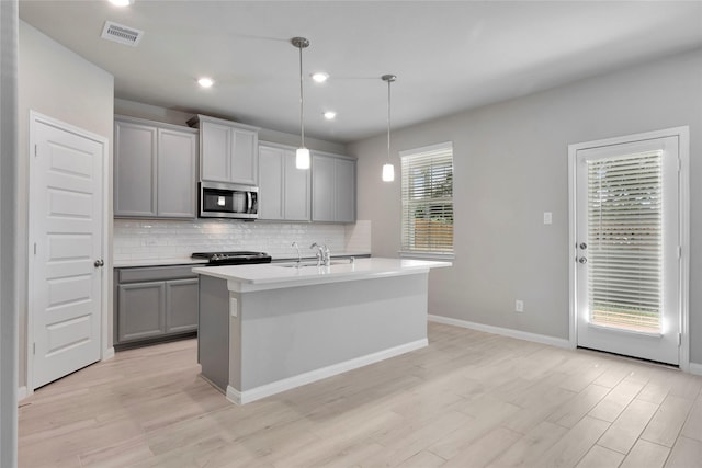 kitchen with gray cabinetry, pendant lighting, a healthy amount of sunlight, and an island with sink